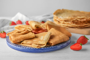 Plate with delicious thin pancakes on table