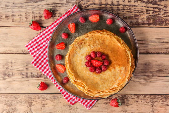 Metal plate with delicious thin pancakes and berries on table