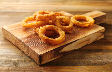 Board with fried breaded onion rings on wooden background