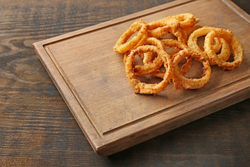 Board with fried breaded onion rings on wooden background