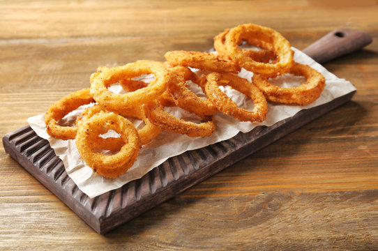 Board with fried breaded onion rings on wooden background