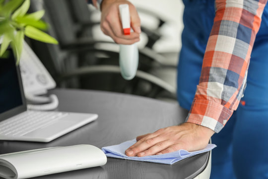 Young man wiping table in office