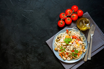 Seafood noodles. Pasta with seafood and vegetables - shrimps, mussels, tomato and spinach on a dark background. Top view