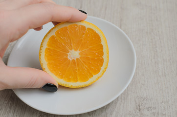 Female hand holds fresh orange slice lying on white saucer, wood background, top view