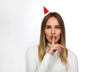 Hübsche blonde Frau mit Weihnachtsmütze und Hand auf den Lippen