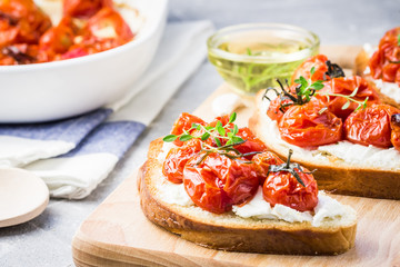 Honey roasted cherry tomatoes bruschetta on light grey concrete background. Selective focus, close up.