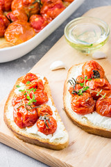 Slow roasted tomatoes and ricotta bruschetta on light grey concrete background. Selective focus, close up.