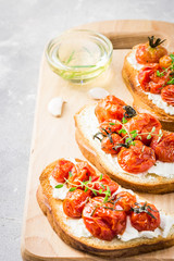 Roasted tomato bruschetta with whipped goat cheese on light grey concrete background. Selective focus, close up.