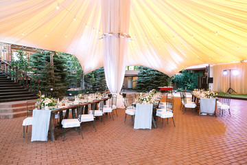 holidays, vacation, setting concept. there is woderful huge white tent under long served tables for celebration of birthday surrounded by always green spruces