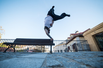 Young man doing handstand on a bench in the street while doing parkour. 
