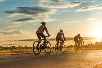 Foto op Plexiglas Group of  men ride  bicycles at sunset with sunbeam over silhouette trees background. © Pattadis