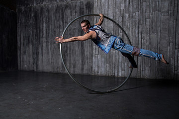 Muscular circus artist in a Cyr Wheel (Roy Cyr) on a gray background