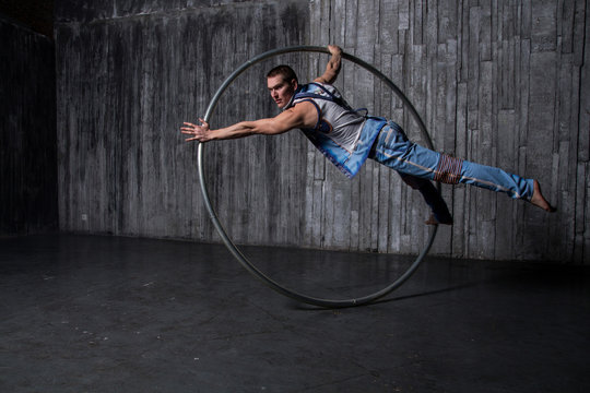 Muscular circus artist in a Cyr Wheel (Roy Cyr) on a gray background