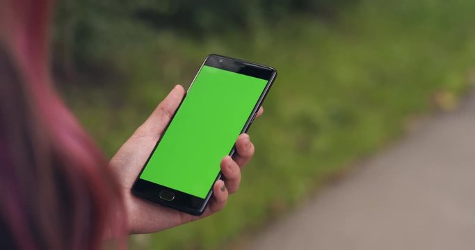 Slow motion handheld shot of teen girl holding smartphone with green screen in summer evening in town