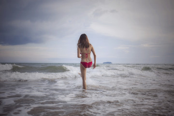 Fototapeta premium The woman in red bikini which stand on beach with the blue sky .There is a cool sea breeze in the air the weather is fin.It is warm and sunny