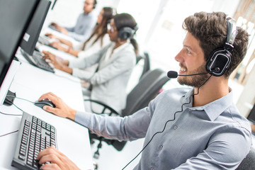 Smiling handsome male customer support phone operator with headset working in call centre.  - obrazy, fototapety, plakaty