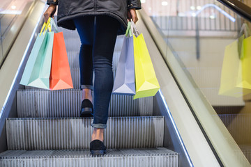 Woman legs with colorful shopping bags on the escalator in a shopping mall