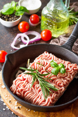 Raw minced beef on a cast iron frying pan, and a variety of spices, vegetables and herbs.