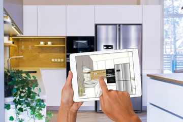 Hands holding tablet with kitchen interior sketch. In the background real finished kitchen interior...
