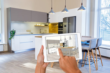 Hands holding tablet with kitchen interior sketch. In the background real finished kitchen interior...