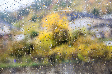 Drops of rain on a window. Blur buildings and trees in background.
