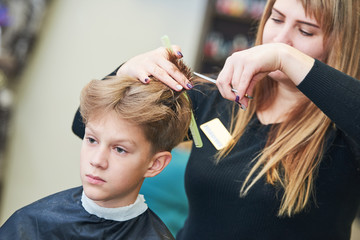 Naklejka premium Barber or hair stylist at work. female hairdresser cutting child hair