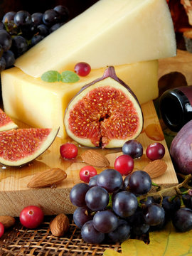 Parmesan on a board surrounded by figs, grapes, cranberries and honey