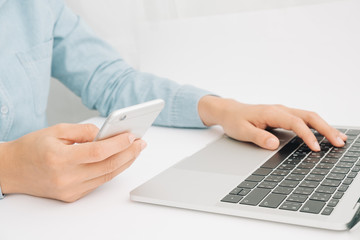 Female using mobile smart phone and working on laptop computer