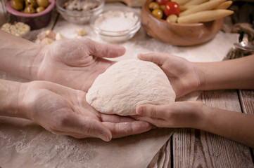 Mother and the daughter cook dough for home-made pizza  on a wooden table. Baking preparing background.