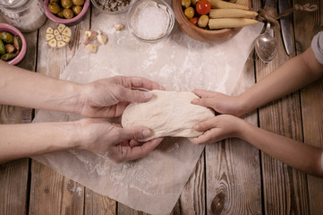 Mother and the daughter cook dough for home-made pizza  on a wooden table. Baking preparing background.