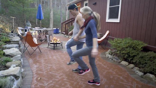 Mature woman and her muscular hip son dance dabka in a relaxed backyard patio atmosphere.