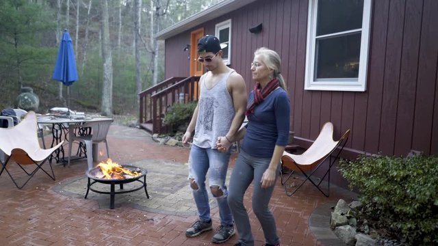 Mother and son hold hands doing some dabke dance moves in their backyard on a warm autumn day with a fire going.