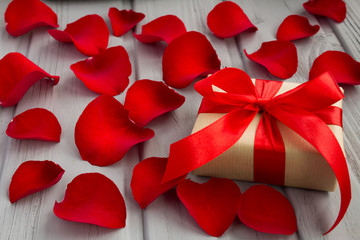 Gift box with the red ribbon and rose petals on the grey  wooden background