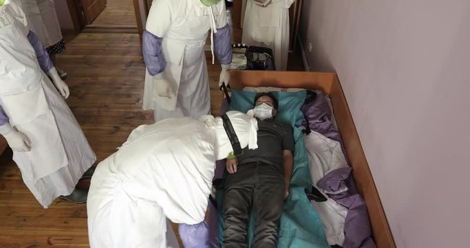 Group of doctors or nurses wearing full Ebola virus protection uniform сarry patient on stretcher. Evacuation and disinfection.