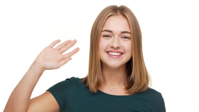 Headshot of friendly female adult with beautiful auburn hair smiling on camera welcoming saying hello waving hand over white background. Concept of emotions