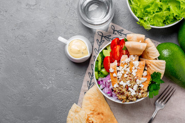 Healthy buddha quinoa salad bowl with tomatoes, cucumbers, red onions chicken and feta cheese. On grey concrete background. Top view copy space.

