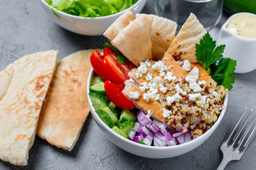 Healthy quinoa salad bowl with tomatoes, cucumbers, red onions chicken and feta cheese. On grey concrete background. Horizontal side view.

