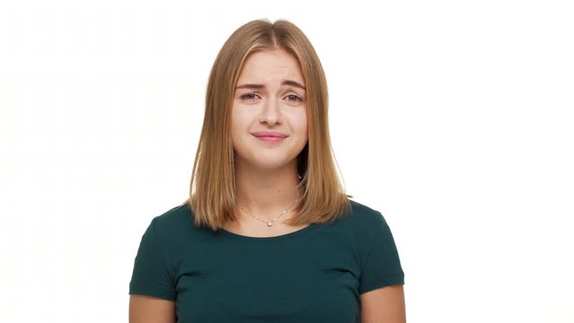 Portrait of candid pleasant woman shrugging meaning don't know biting lips posing over white background with doubtful expressions. Concept of emotions