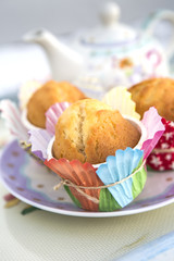 magdalenas con papelillos de colores en plato adornado y al fondo una tetera difuminada.