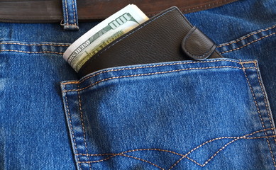 black leather wallet with money dollars sticking out of jeans pocket