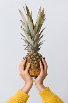 Closeup of fresh pineapple in woman's hands on light blue background.
