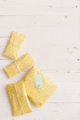Top view on small gifts wrapped in yellow paper with ribbons and tag on white wooden background. Presents for birthday, Christmas or any other celebration.