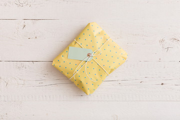 Top view on small wrapped gift with ribbons and tag on white wooden background. Present for birthday, Christmas or any other celebration or party