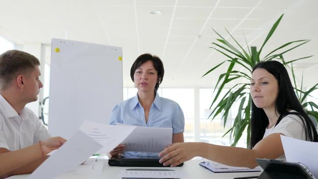 Business meeting of collaborators at desk with documents in hand in boardroom with large windows