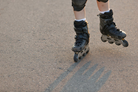Closeup of child's legs in roller skates. Boy rollerblading on asphalt road on sunny day. Activities and sports outdoor. Lifestyle