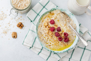 Oatmeal porridge with fresh raspberries, walnuts and butter in a ceramic plate on a light stone or concrete background. Selective focus.