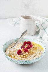 Oatmeal porridge with fresh raspberries, walnuts and butter in a ceramic plate on a light stone or concrete background. Selective focus.