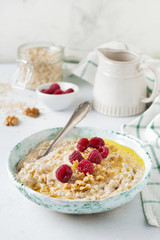 Oatmeal porridge with fresh raspberries, walnuts and butter in a ceramic plate on a light stone or concrete background. Selective focus.