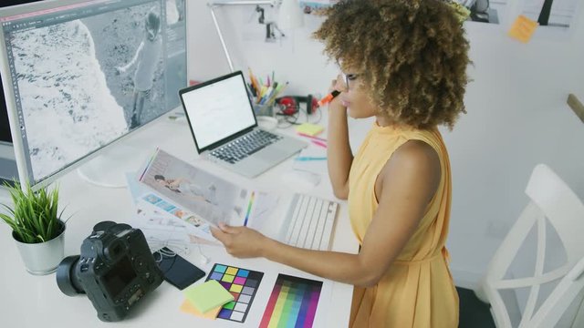 Young successful businesswoman in trendy clothing posing at desktop with computer and exploring photos working as creative designer.