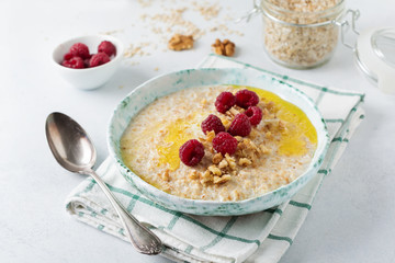 Oatmeal porridge with fresh raspberries, walnuts and butter in a ceramic plate on a light stone or concrete background. Selective focus.